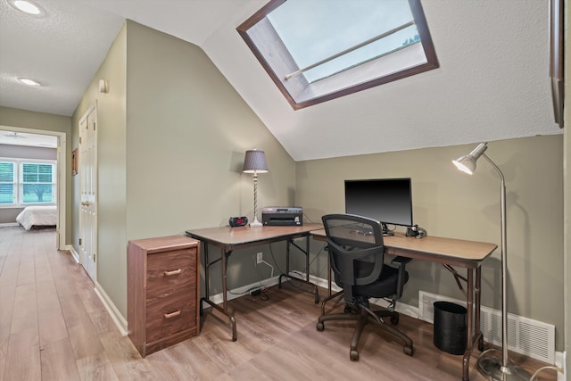 home office featuring vaulted ceiling with skylight, a textured ceiling, and light wood-type flooring