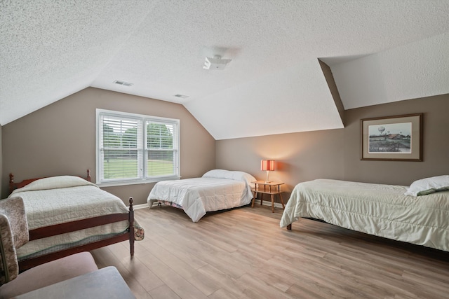 bedroom featuring a textured ceiling, lofted ceiling, and light hardwood / wood-style flooring