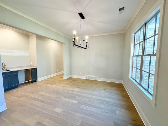 unfurnished dining area featuring a chandelier, light wood-type flooring, ornamental molding, and sink