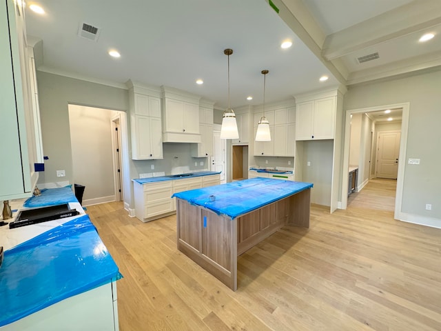 kitchen featuring a kitchen island, light hardwood / wood-style flooring, pendant lighting, white cabinets, and ornamental molding