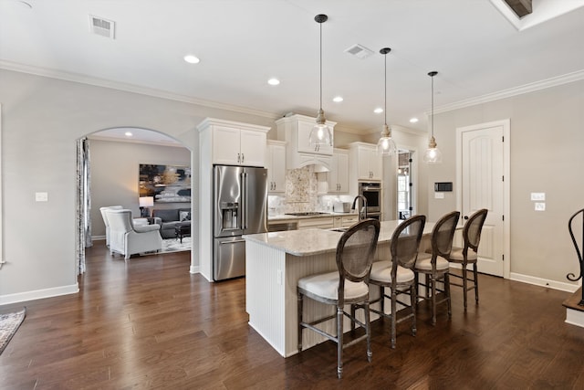 kitchen with appliances with stainless steel finishes, white cabinetry, decorative light fixtures, light stone counters, and a kitchen island with sink