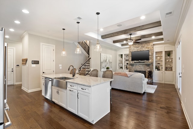 kitchen with a kitchen island with sink, beamed ceiling, sink, pendant lighting, and white cabinets