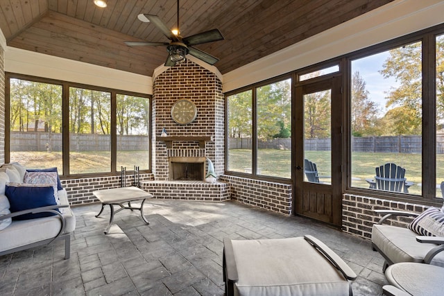 sunroom featuring vaulted ceiling, wood ceiling, a brick fireplace, and ceiling fan