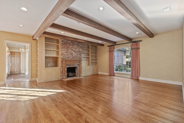 unfurnished living room featuring beam ceiling, built in features, light hardwood / wood-style flooring, and a fireplace