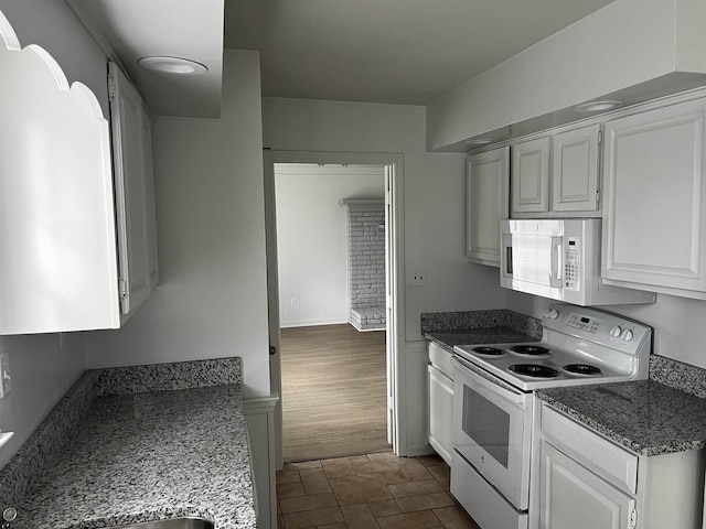 kitchen featuring white cabinetry, dark stone counters, and white appliances