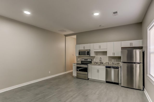 kitchen with a sink, baseboards, white cabinets, light wood-style floors, and stainless steel appliances