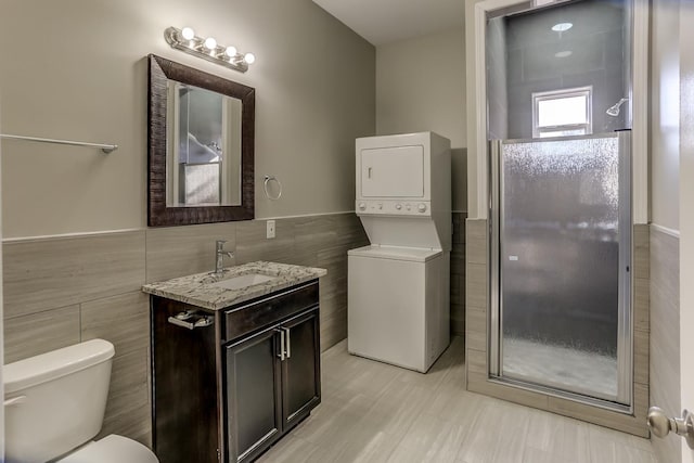 full bath with tile walls, stacked washer and clothes dryer, a shower stall, and a wainscoted wall