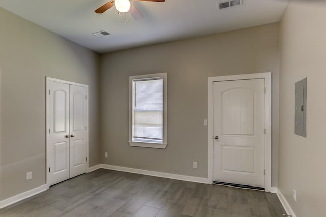 spare room with electric panel, a ceiling fan, wood finished floors, and visible vents