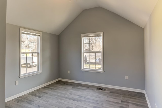 additional living space with baseboards, visible vents, wood finished floors, and lofted ceiling