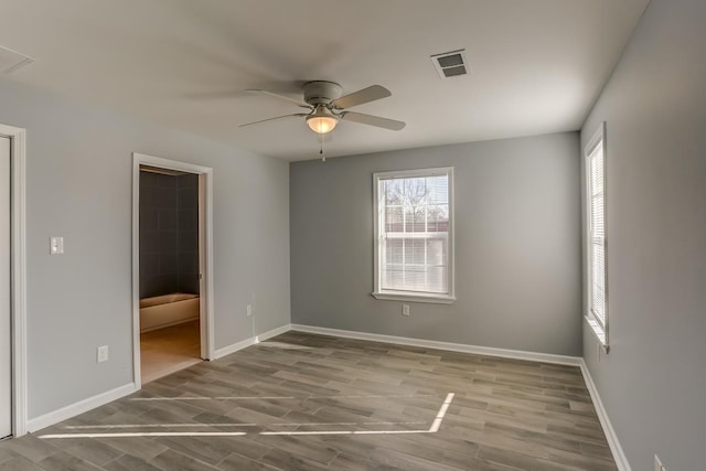 unfurnished bedroom featuring a ceiling fan, baseboards, wood finished floors, ensuite bathroom, and visible vents