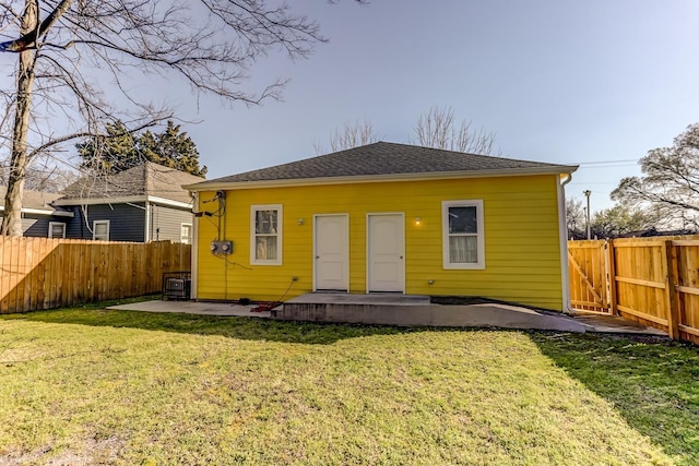 rear view of property with a patio, a fenced backyard, roof with shingles, and a yard