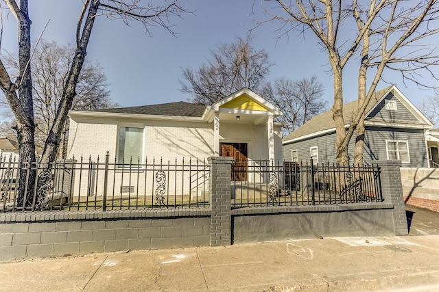 view of front facade featuring brick siding, a fenced front yard, and roof with shingles