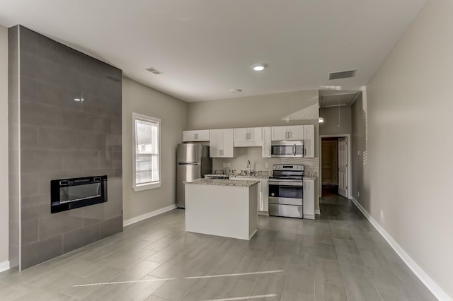 kitchen featuring white cabinets, a sink, a tiled fireplace, stainless steel appliances, and visible vents