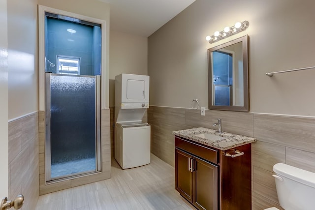 bathroom with wainscoting, stacked washer / drying machine, toilet, and tile walls