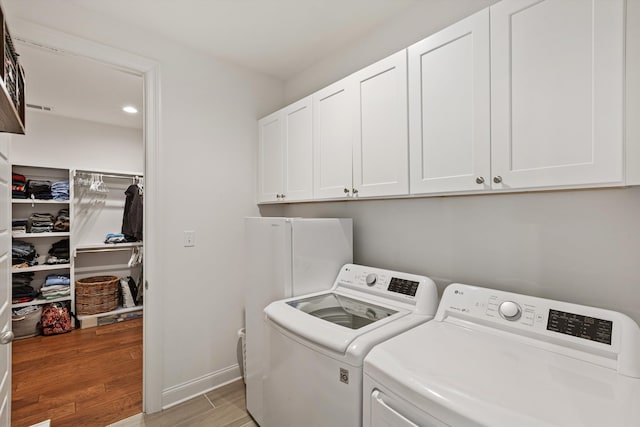 clothes washing area featuring washer and clothes dryer, light hardwood / wood-style flooring, and cabinets