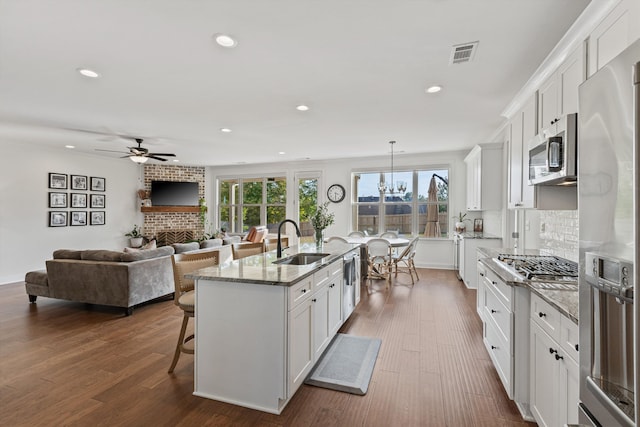 kitchen with sink, dark hardwood / wood-style flooring, stainless steel appliances, white cabinets, and a center island with sink