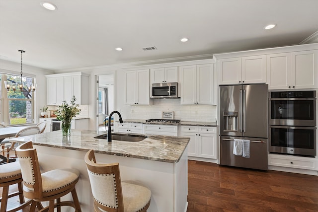 kitchen with an island with sink, white cabinetry, sink, pendant lighting, and stainless steel appliances