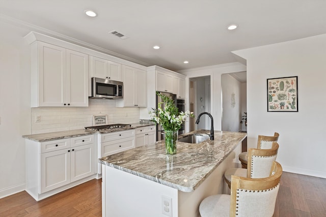 kitchen featuring a center island with sink, sink, stainless steel appliances, and wood-type flooring