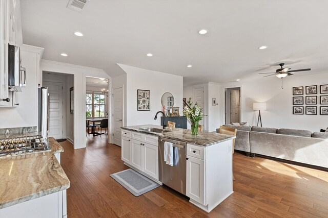 kitchen with dark hardwood / wood-style floors, stainless steel appliances, a center island with sink, light stone countertops, and white cabinetry