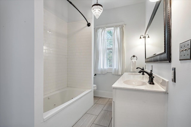 full bathroom featuring toilet, tiled shower / bath, vanity, and a notable chandelier