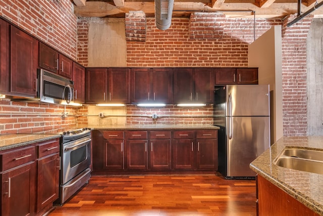 kitchen featuring light stone counters, brick wall, appliances with stainless steel finishes, and dark hardwood / wood-style floors