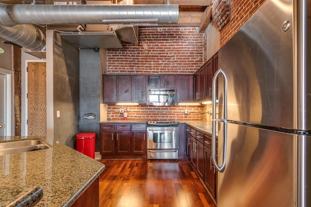 kitchen featuring dark wood-type flooring, brick wall, sink, stone counters, and appliances with stainless steel finishes