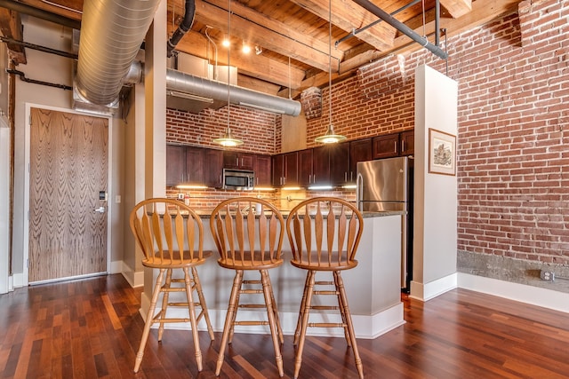 kitchen featuring beam ceiling, appliances with stainless steel finishes, wooden ceiling, a towering ceiling, and brick wall