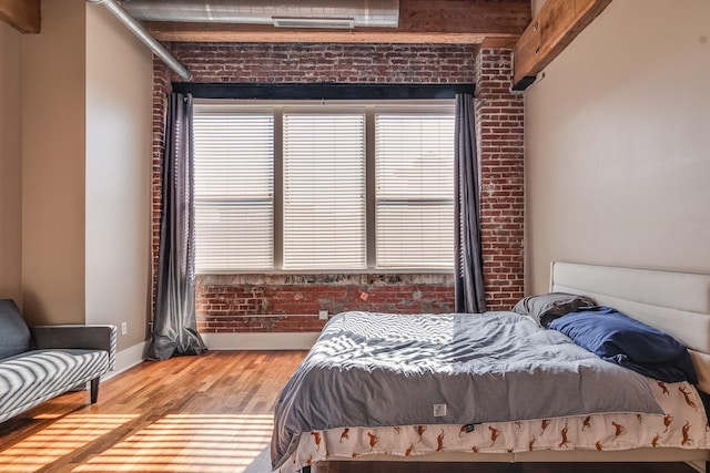 bedroom featuring beamed ceiling, brick wall, and hardwood / wood-style floors