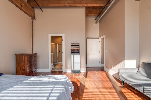 bedroom featuring beam ceiling, a high ceiling, ensuite bathroom, and wood-type flooring