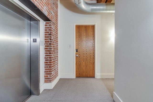 hallway featuring light colored carpet, brick wall, and elevator