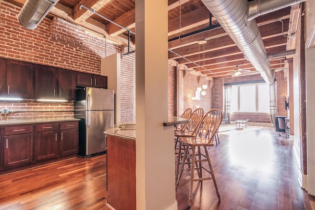 kitchen with hardwood / wood-style flooring, brick wall, stainless steel refrigerator, and beamed ceiling