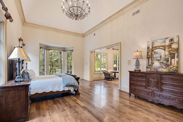 bedroom featuring a notable chandelier, hardwood / wood-style flooring, ornamental molding, and a high ceiling