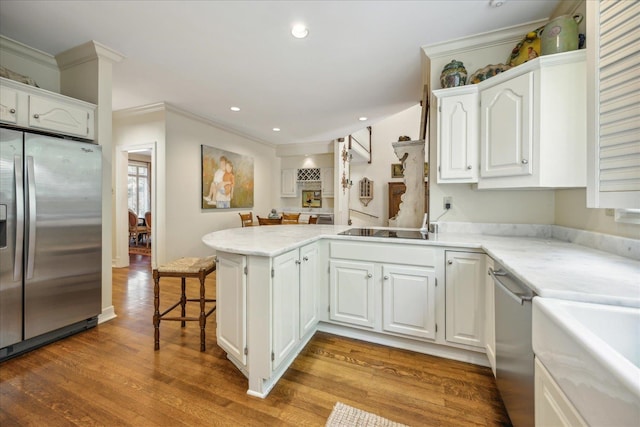 kitchen with appliances with stainless steel finishes, kitchen peninsula, white cabinets, and hardwood / wood-style flooring