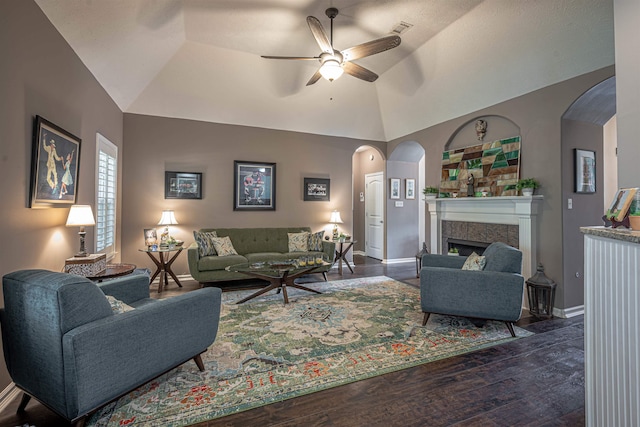 living room featuring dark hardwood / wood-style floors, vaulted ceiling, ceiling fan, and a tiled fireplace