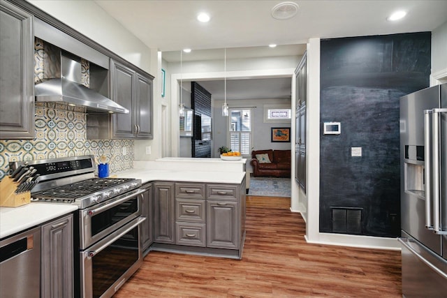 kitchen featuring decorative backsplash, wall chimney exhaust hood, kitchen peninsula, hardwood / wood-style floors, and appliances with stainless steel finishes