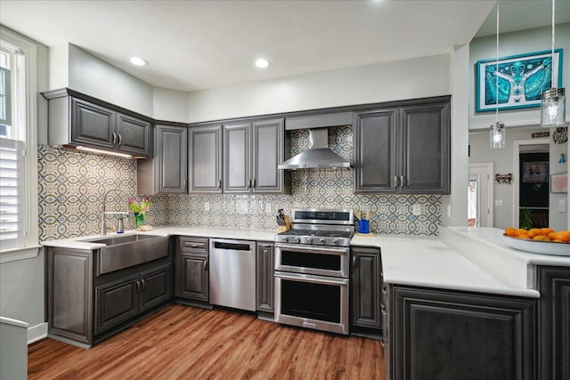 kitchen featuring wall chimney range hood, hardwood / wood-style flooring, appliances with stainless steel finishes, and a wealth of natural light