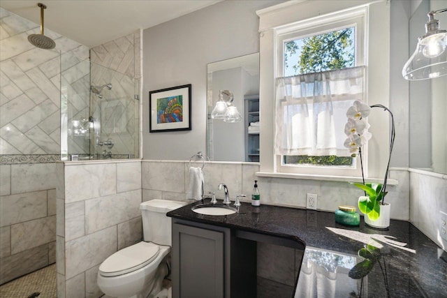 bathroom featuring vanity, toilet, tile walls, and tiled shower