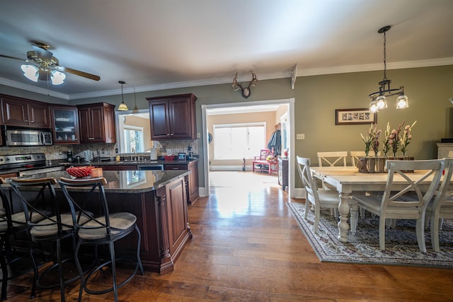 kitchen with tasteful backsplash, ceiling fan with notable chandelier, stainless steel appliances, dark stone counters, and dark wood-type flooring