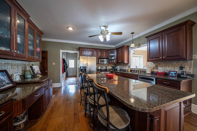 kitchen featuring appliances with stainless steel finishes, a kitchen island, decorative light fixtures, decorative backsplash, and dark hardwood / wood-style floors