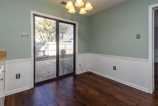 unfurnished dining area with a textured ceiling, dark hardwood / wood-style flooring, and an inviting chandelier