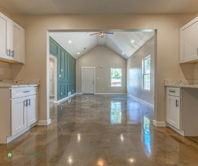 kitchen featuring light stone countertops, vaulted ceiling, white cabinets, and ceiling fan