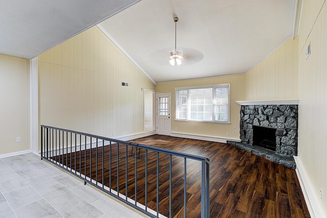 unfurnished living room with a baseboard heating unit, wood-type flooring, vaulted ceiling, a stone fireplace, and crown molding