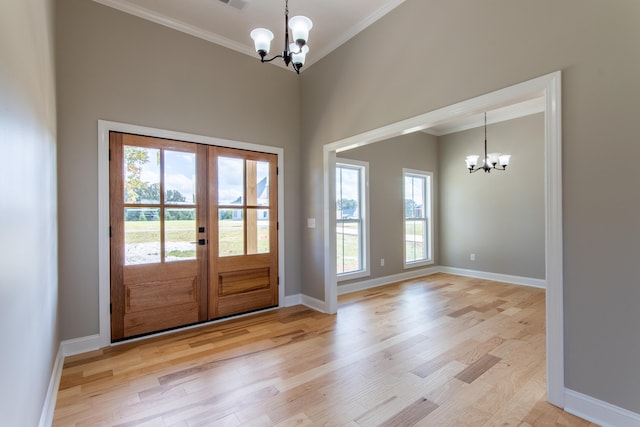 doorway with ornamental molding, a notable chandelier, french doors, and light wood-type flooring