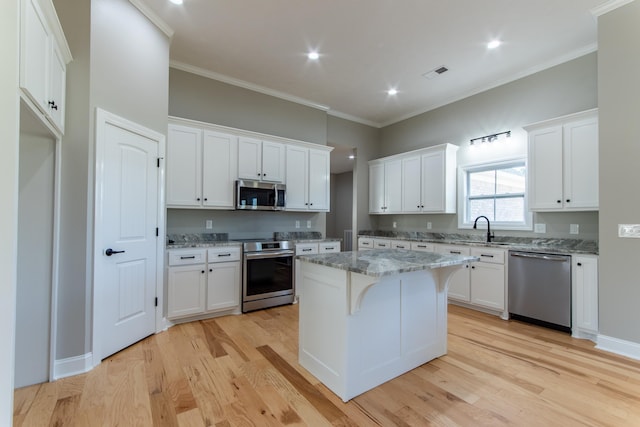 kitchen with white cabinets, a kitchen island, appliances with stainless steel finishes, light stone countertops, and light hardwood / wood-style floors