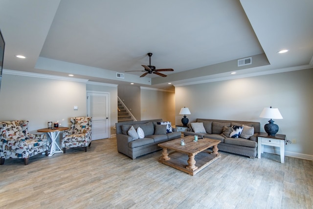 living room featuring crown molding, a raised ceiling, light hardwood / wood-style floors, and ceiling fan