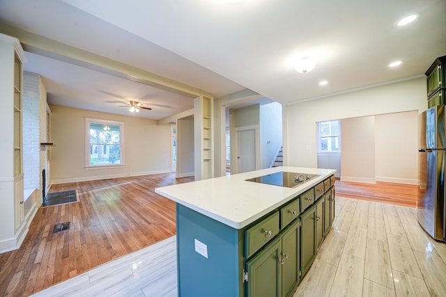 kitchen with light hardwood / wood-style floors, stainless steel refrigerator, green cabinetry, and an island with sink