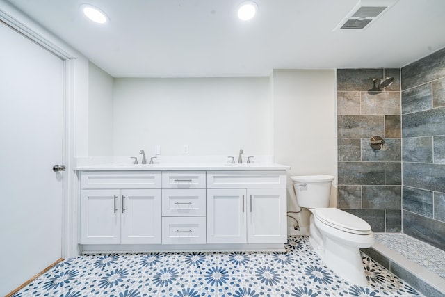 bathroom with toilet, tile patterned flooring, vanity, and tiled shower