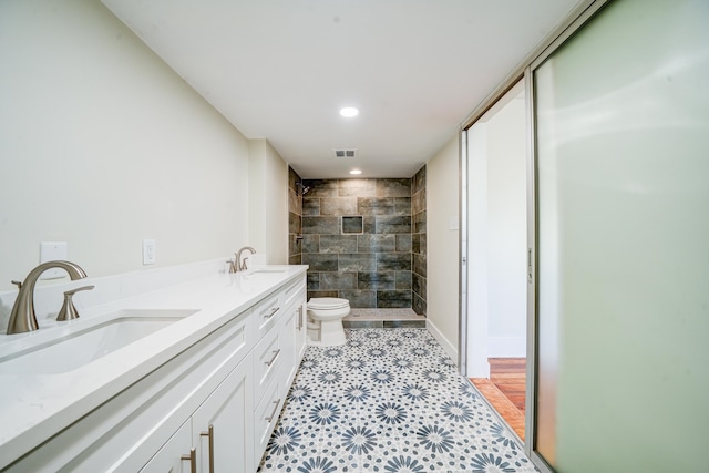 bathroom with a tile shower, toilet, and vanity