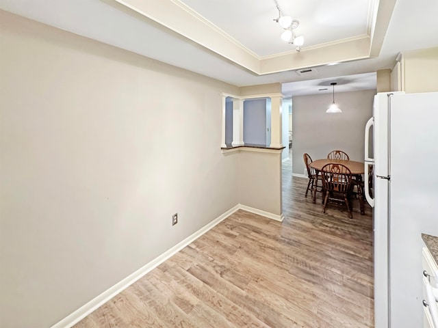 kitchen with ornamental molding, hanging light fixtures, a raised ceiling, white refrigerator, and light wood-type flooring