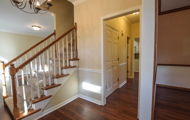 stairway with crown molding, wood-type flooring, and an inviting chandelier